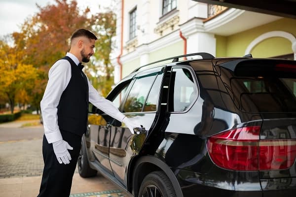 Professional chauffeur standing beside executive vehicle